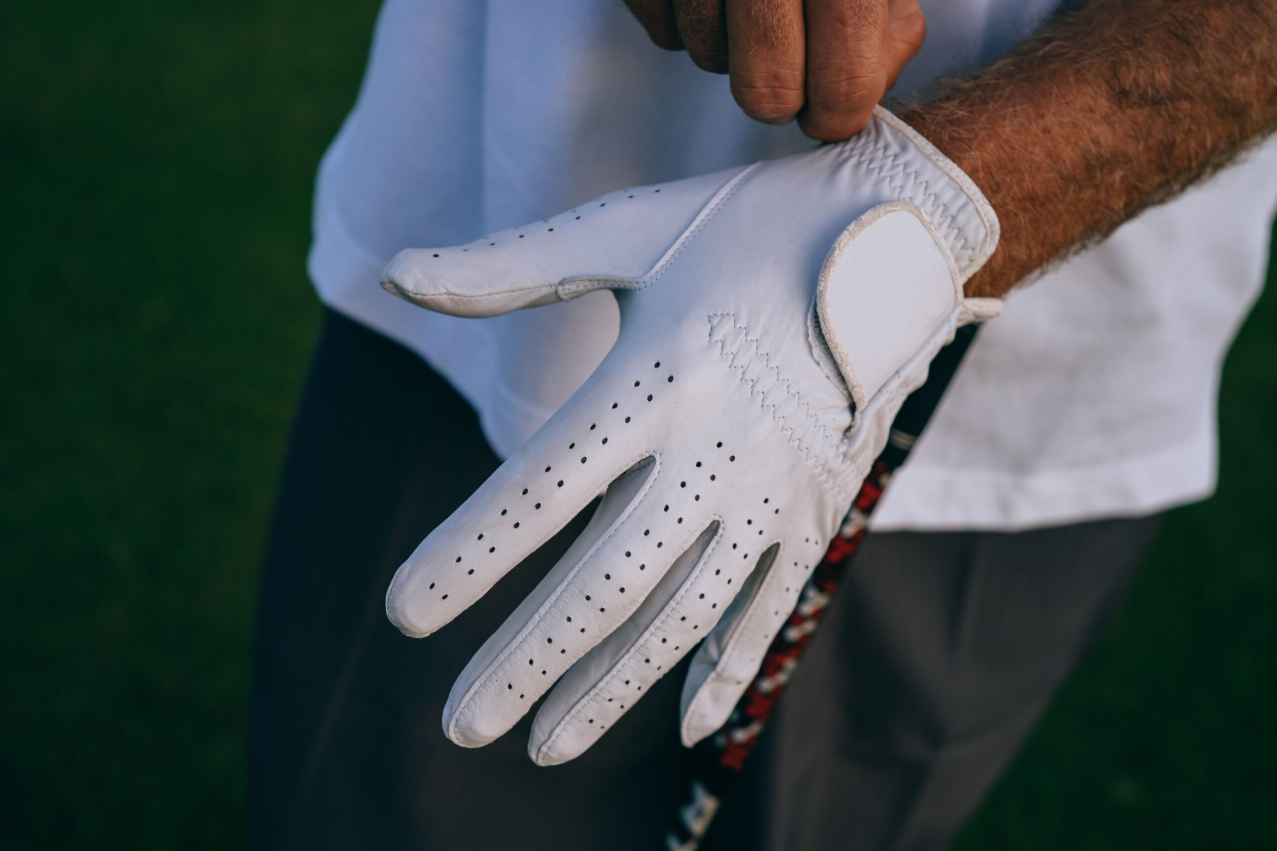 Golfer adjusting a glove while holding a club